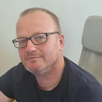 David sitter i en kontorsstol och ler lätt, klädd i glasögon och mörk t-shirt.