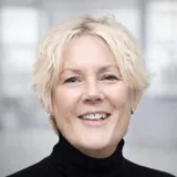 Susanne Wallerstein ler mot kameran, klädd i svart polotröja, mot en ljus och suddig kontorsbakgrund.