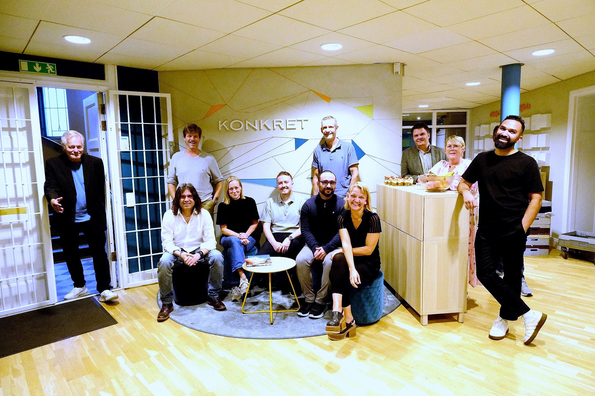 Medarbetarna på Konkret samlade på kontoret framför en vägg med Konkrets logotyp